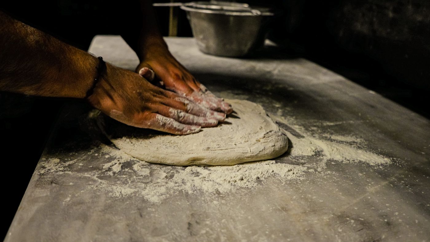 Mains qui travaillent une pâte à pizza sur un plan fariné
